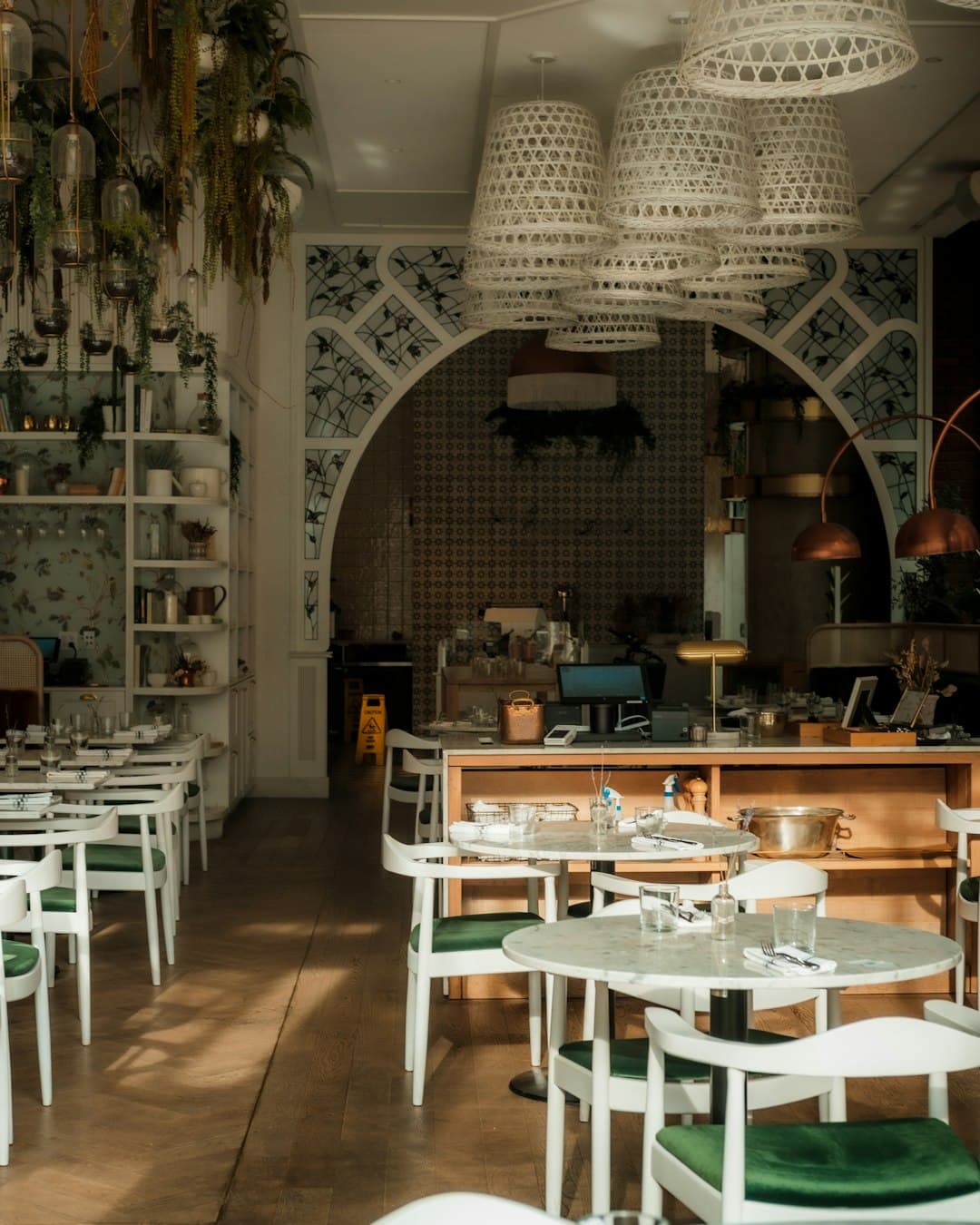 A bright breakfast room of marble tables and green chairs under woven pendant lamps.