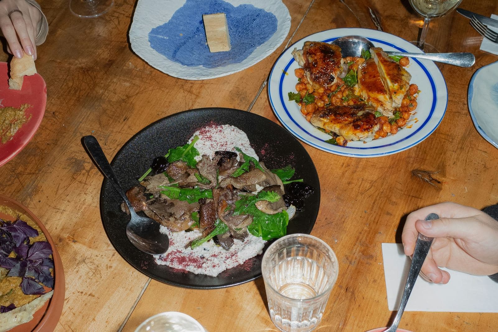 An overhead view of a shared table, plates of fish, salad and dips between reaching hands.